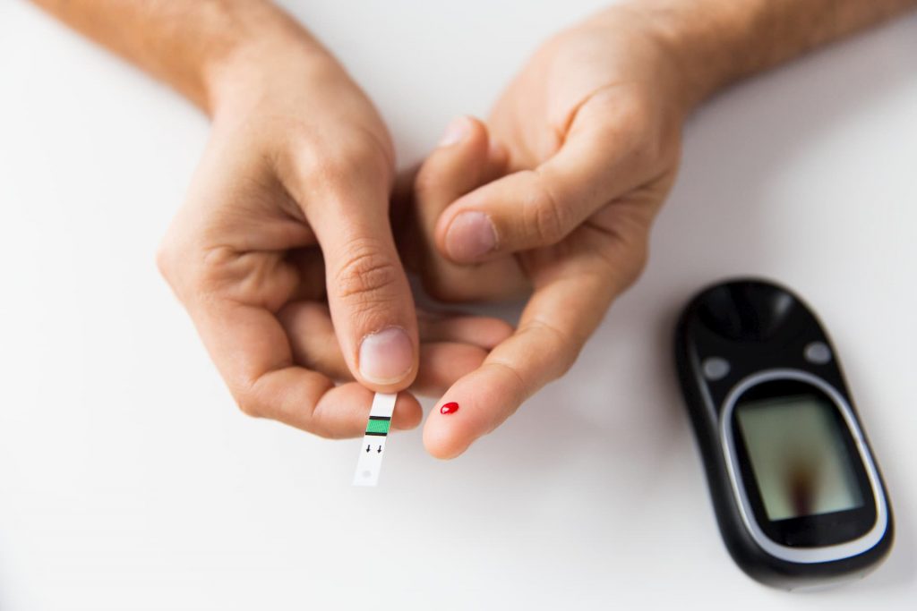Person checking blood glucose with blood on finger and strip in hand next to blood glucose monitor