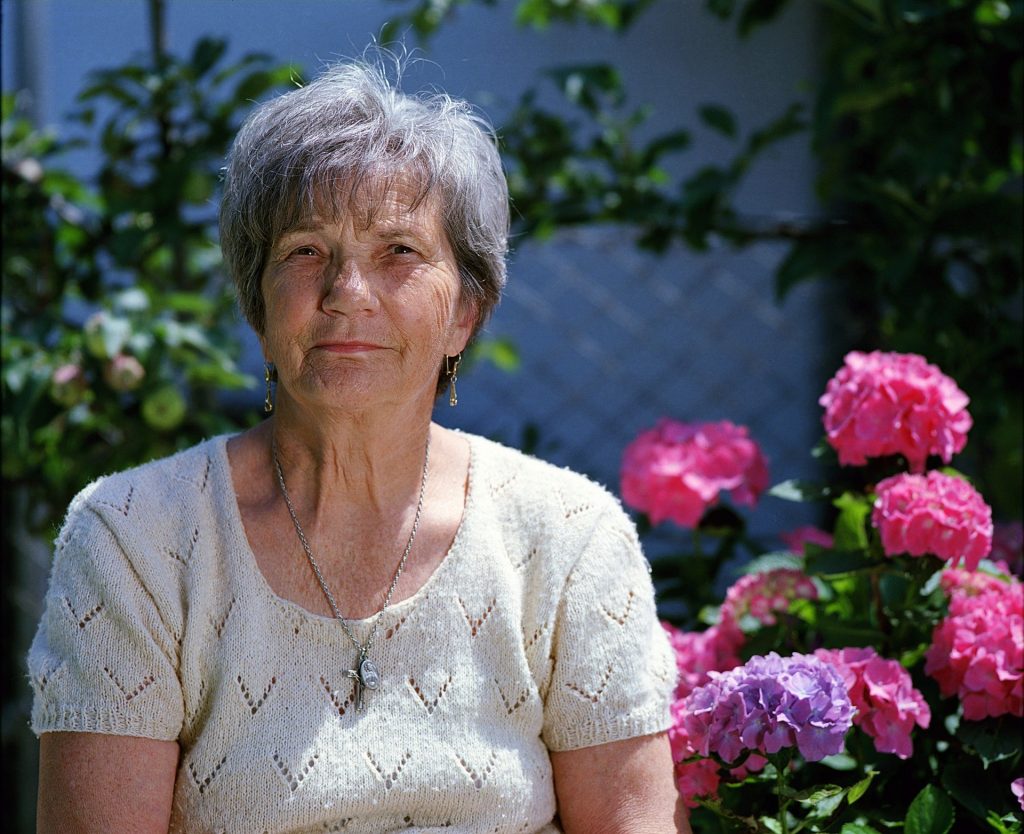 older woman sitting in front of flower garden