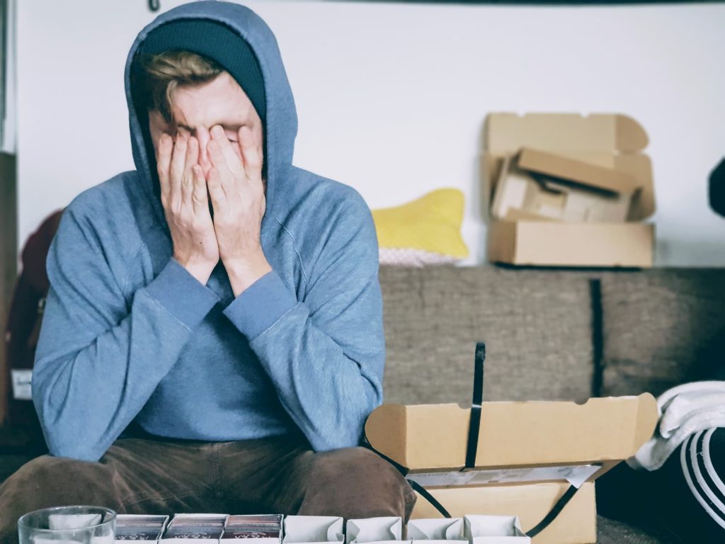 white boy in blue hoodie with hands on face and fingers in eyes looking stressed