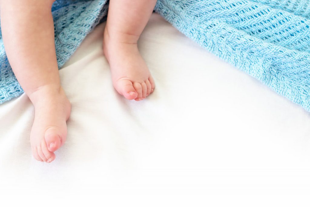 Baby feet with blue blanket; safe sleep is crucial in reducing the risk of SIDS/SUID.