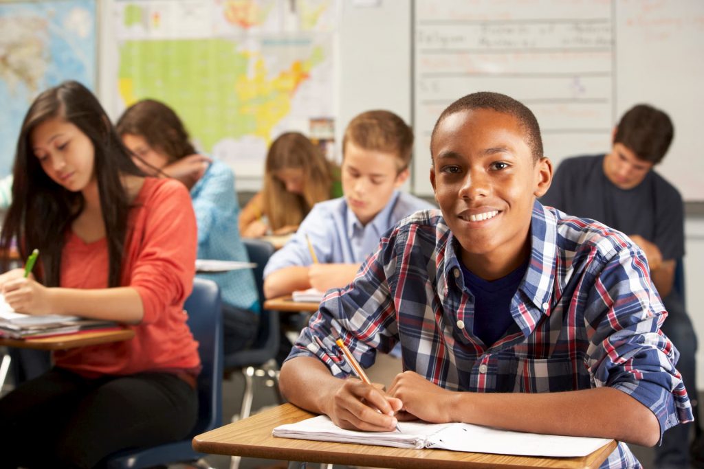 Group of kids sitting in class at desk working on homework and smiling