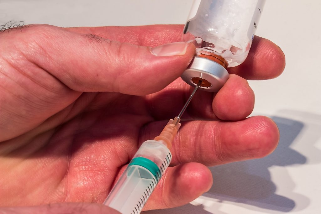 doctor pulling vaccine out of vial with needle and syringe.