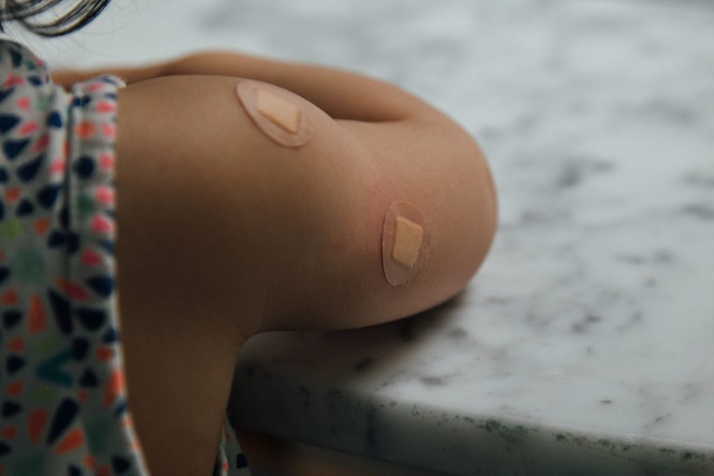 Child with two bandaids on right arm after getting vaccine shots