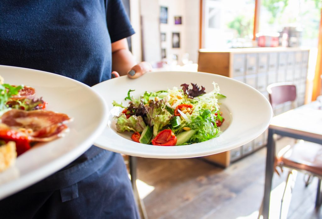 waitress carrying two bowls of salad with leafy greens and tomatoes and mixed veggies on top as a healthy food option