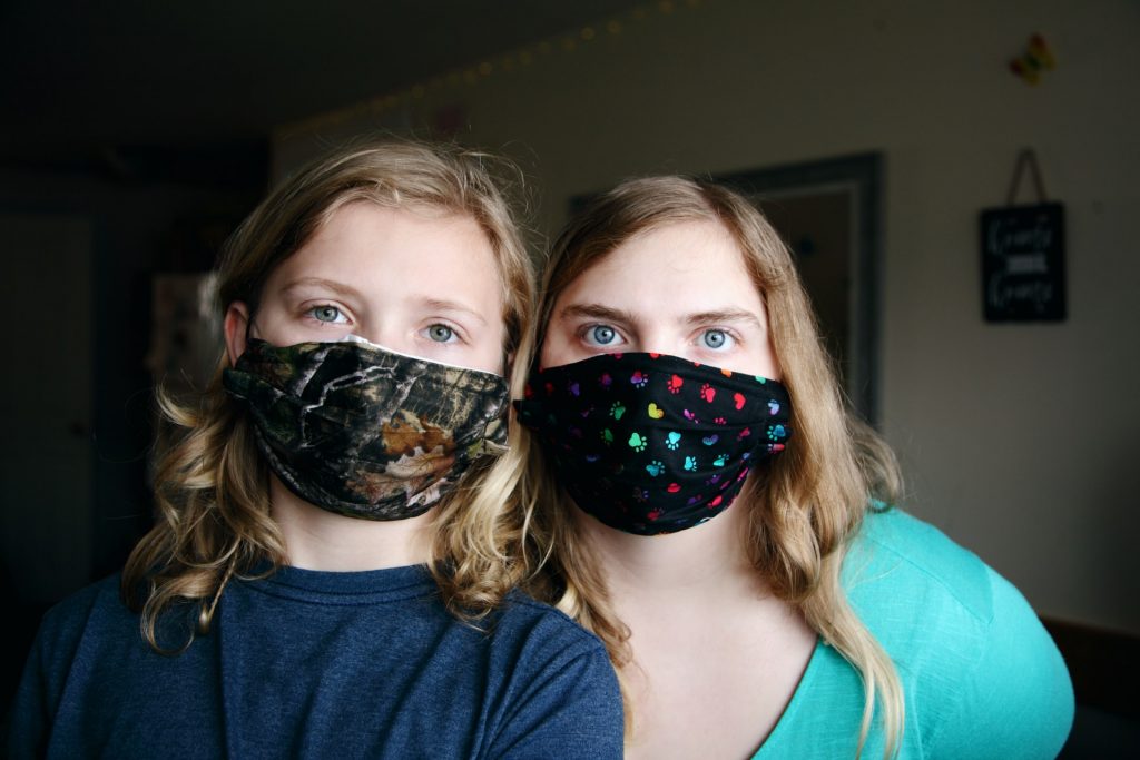 Mother daughter wear cloth masks per CDC guidelines. One mask with RealTree camo print and the other with paws and hearts to protect each other from COVID-19 pandemic