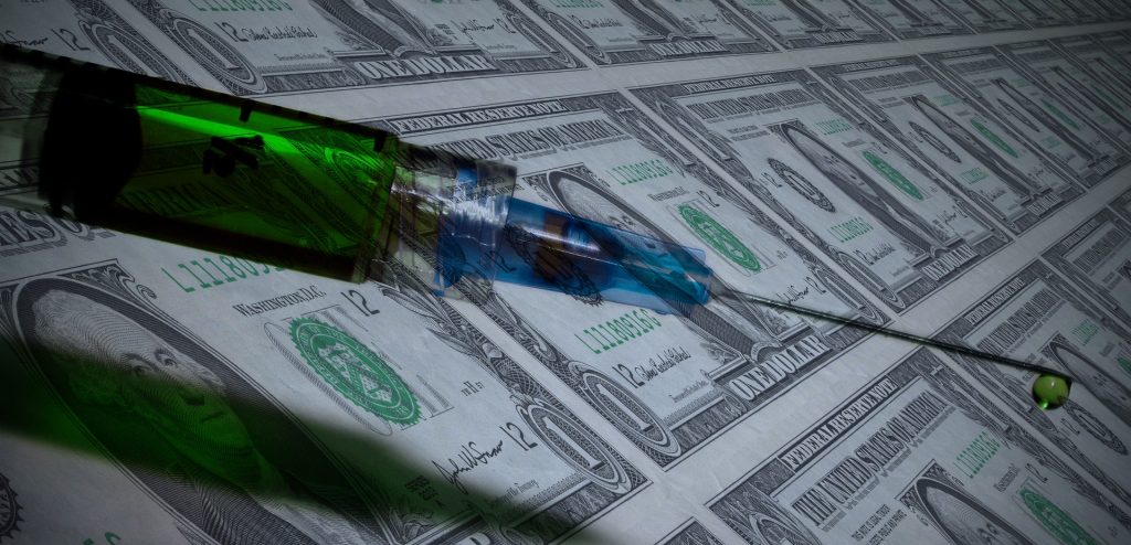 needle with green liquid vaccine inside over a background of money
